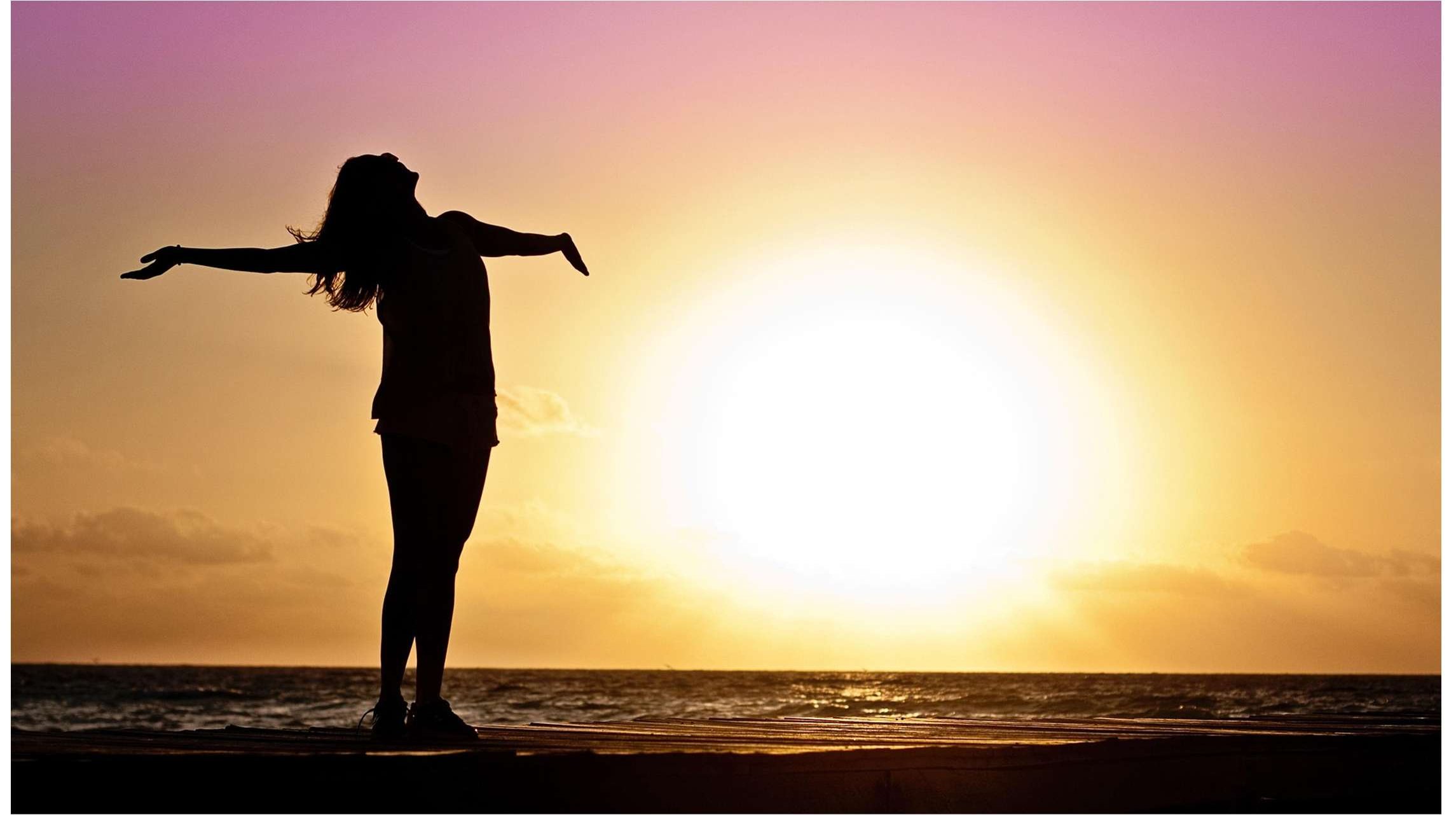 A woman stands with arms outstretched, silhouetted against a sunrise over the water.